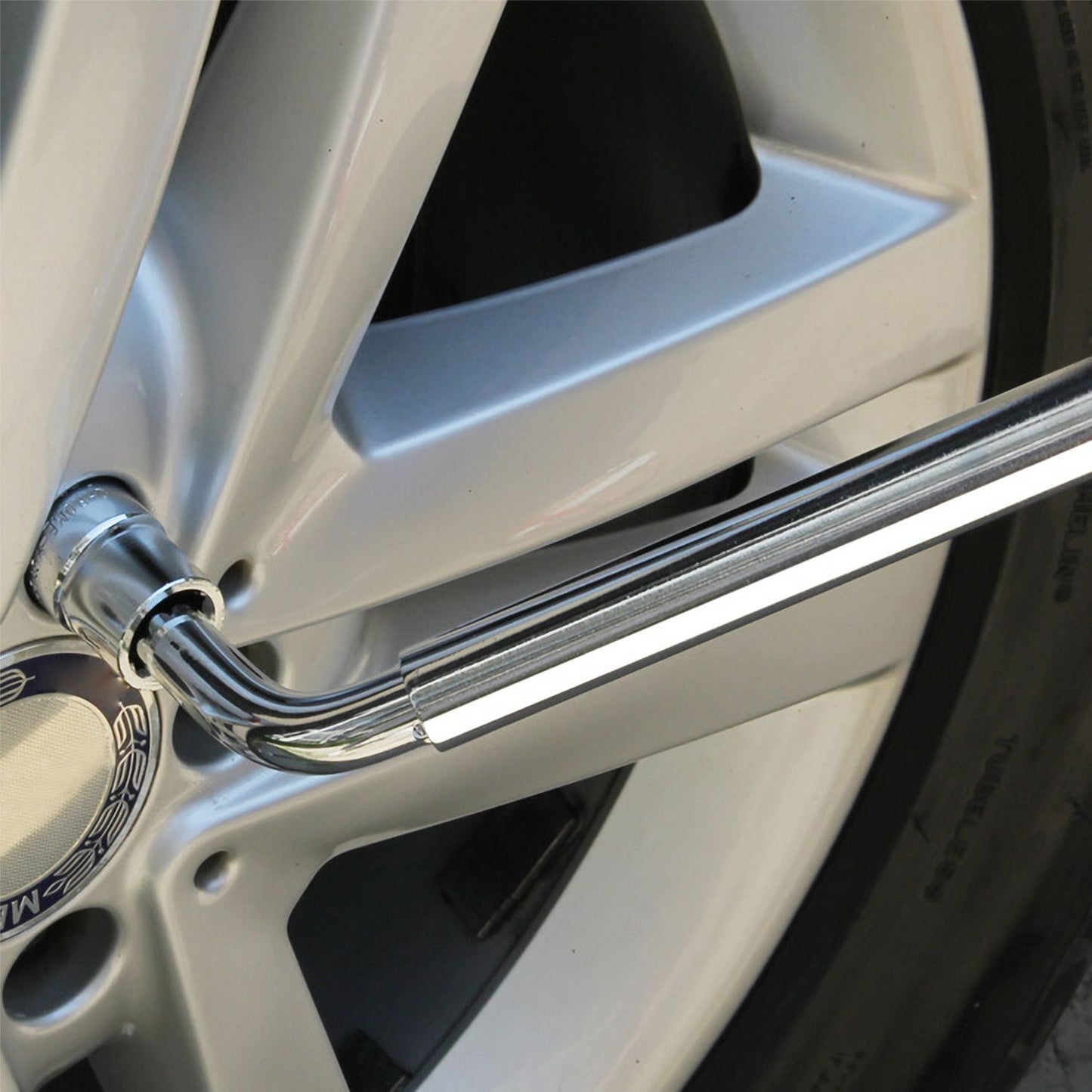 Close-up of a shiny chrome lug wrench engaged with a car wheel, highlighting the intricate details of the wheel rim and tire.