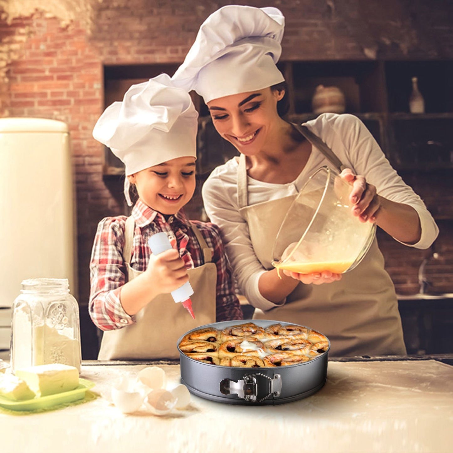 A mother and child in matching chef hats prepare a delicious cinnamon roll cake in a modern kitchen, featuring a springform pan filled with baked goods, surrounded by baking ingredients like eggs and flour.