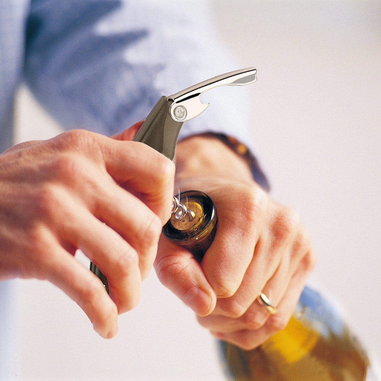 Close-up of a person using a corkscrew wine opener to uncork a bottle, showcasing the tool's sleek design and ease of use.
