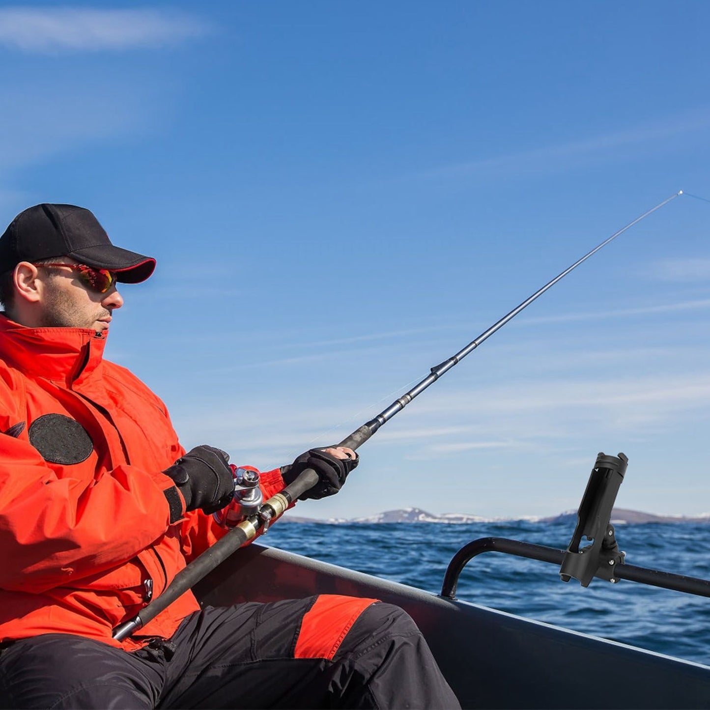 Fisherman in bright orange jacket seated in a boat, casting a fishing rod against a clear blue sky and calm water.