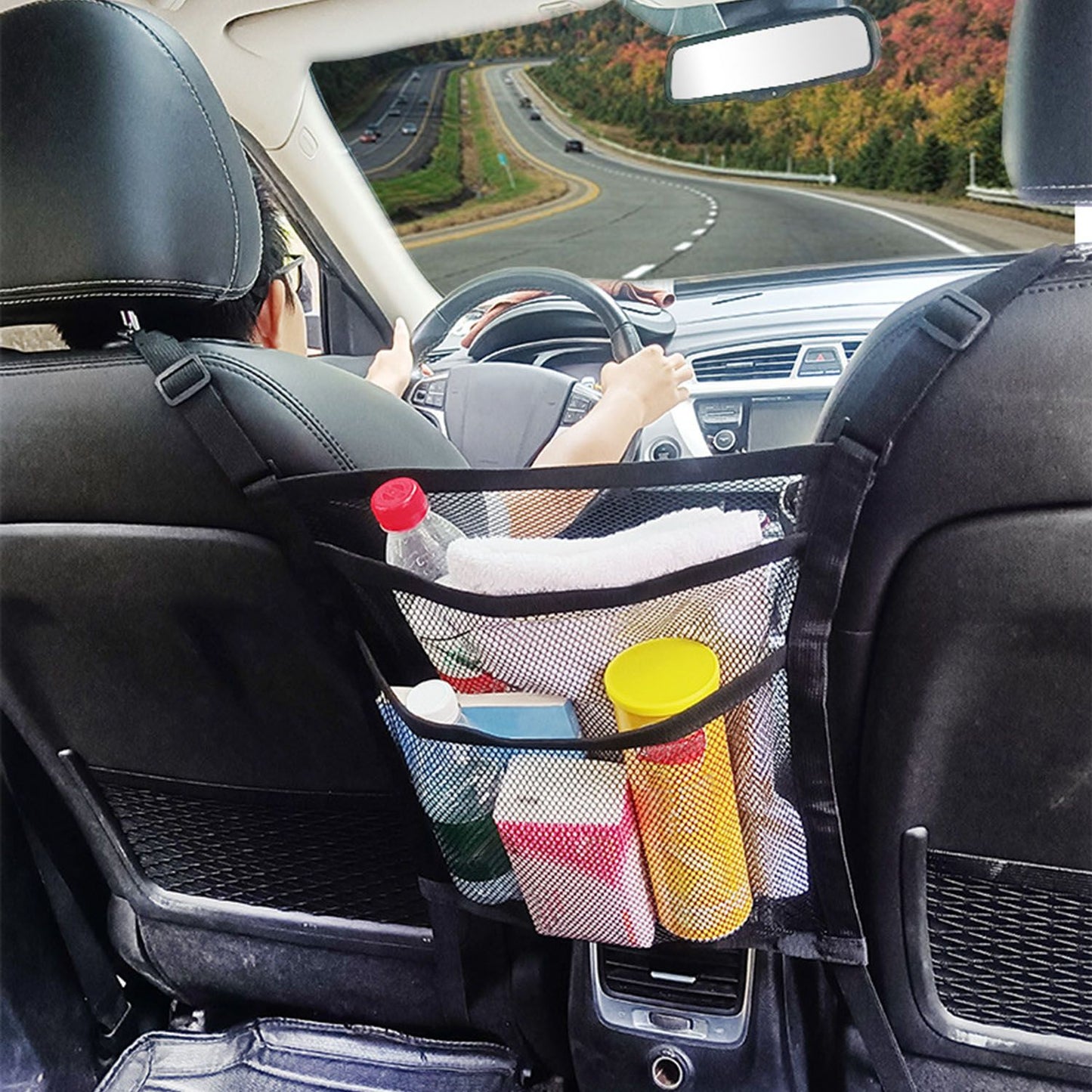 Car backseat organizer with multiple compartments holding drinks, towels, and cleaning supplies, featuring a view of a scenic road ahead.