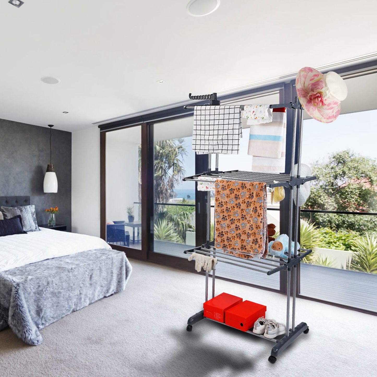 Indoor folding clothes drying rack with freshly laundered towels and clothing in a modern bedroom with large glass windows showcasing a green landscape.