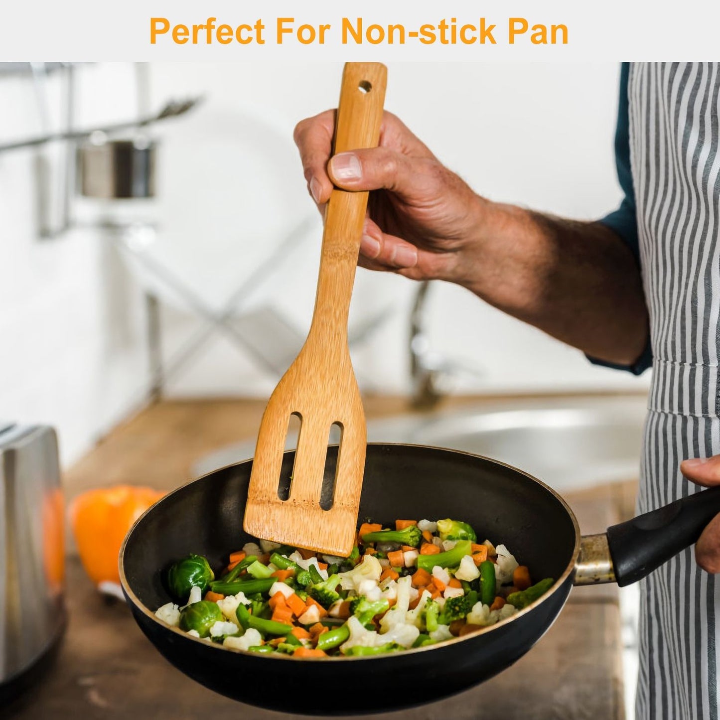 Hand holding a bamboo spatula while cooking colorful sautéed vegetables in a non-stick pan, showcasing a modern kitchen setting.