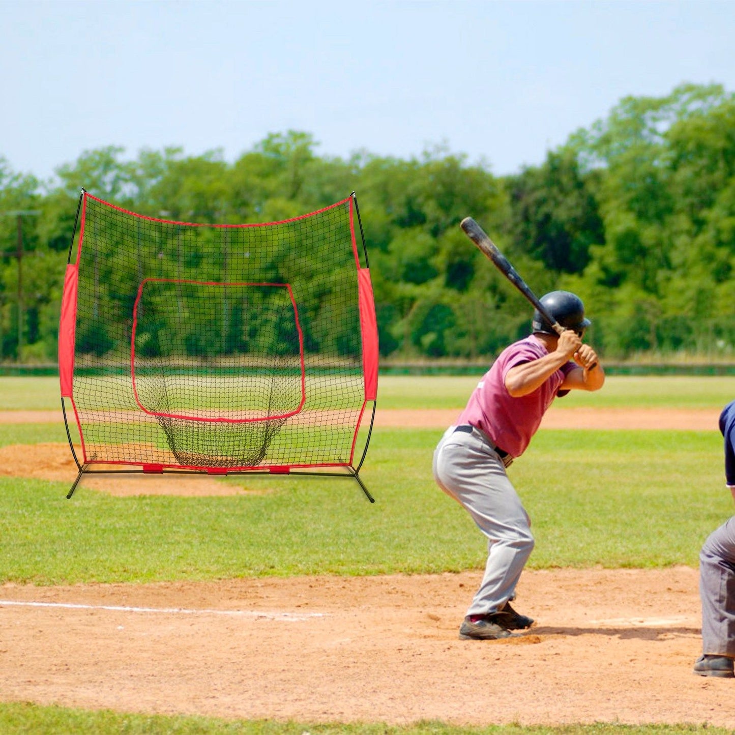 Baseball player in a maroon shirt and black helmet preparing to bat in front of a portable batting practice net on an outdoor field.