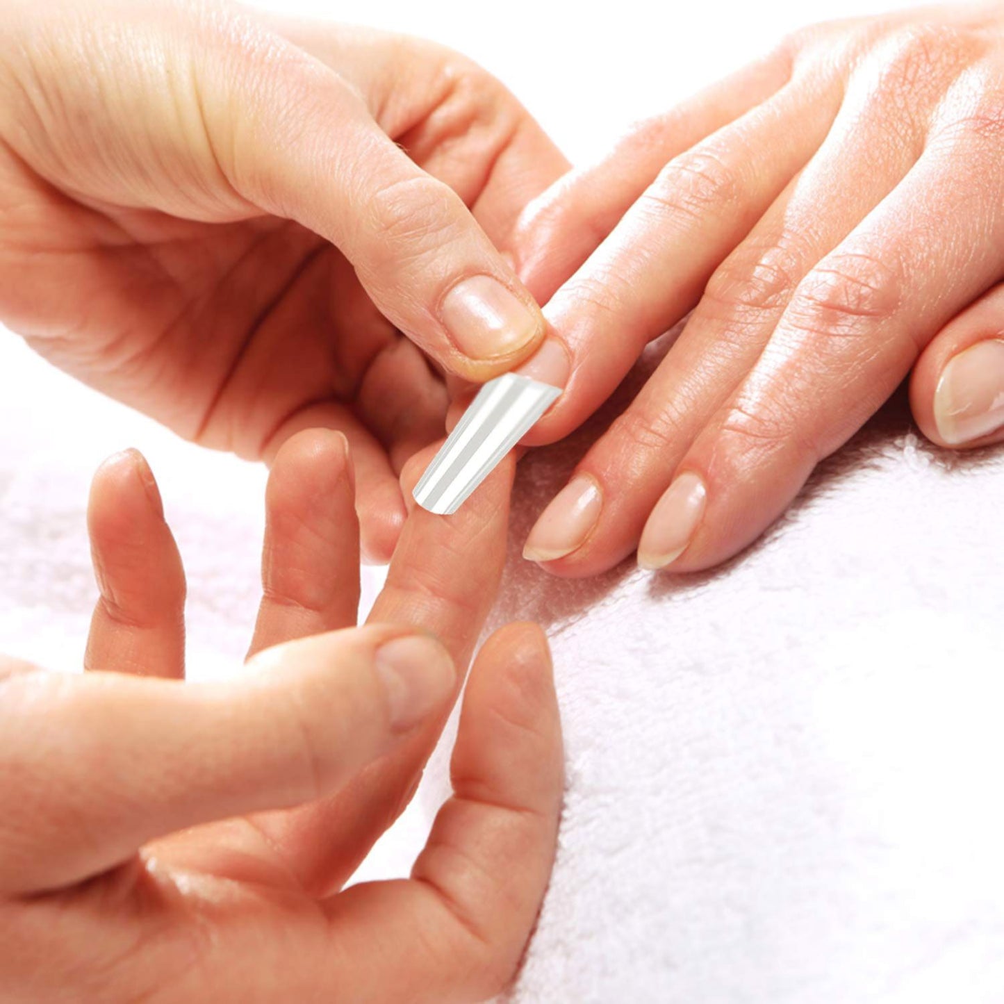 Close-up of a manicure process, showcasing a technician applying a nail form to a client's finger for nail enhancement on a soft towel background.