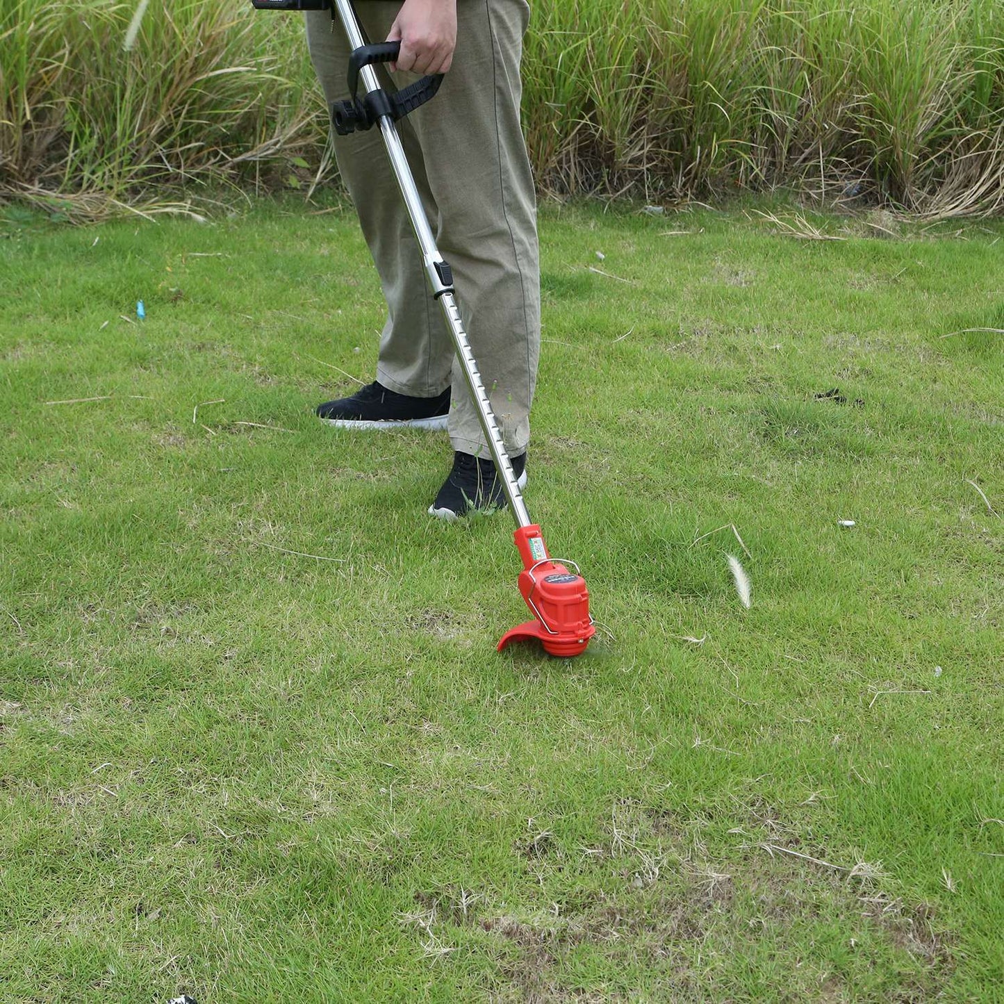 Man using a red electric string trimmer to cut grass on a green lawn.
