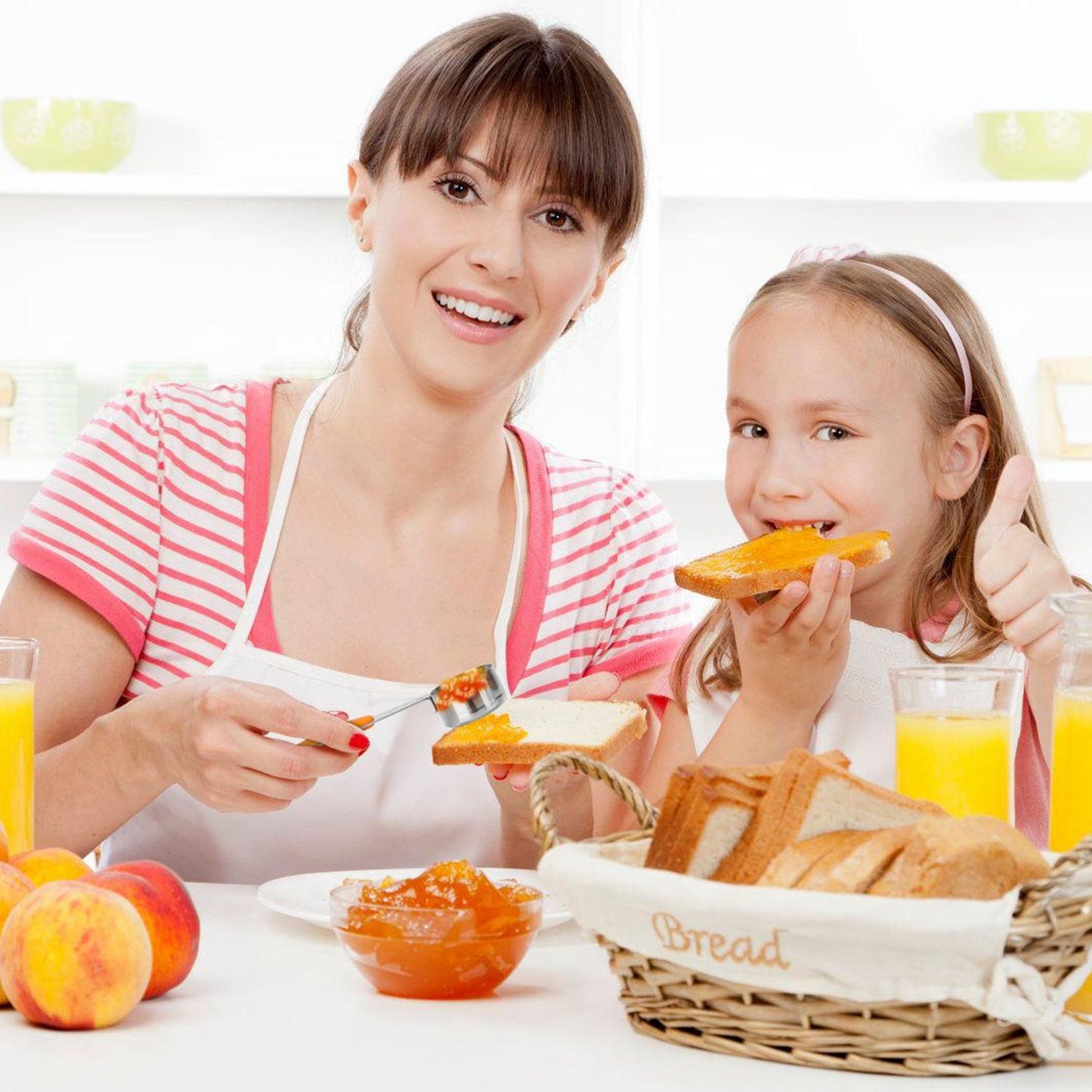 A mother and daughter enjoying breakfast together, spreading jam on toast with fresh fruit and orange juice on the table.