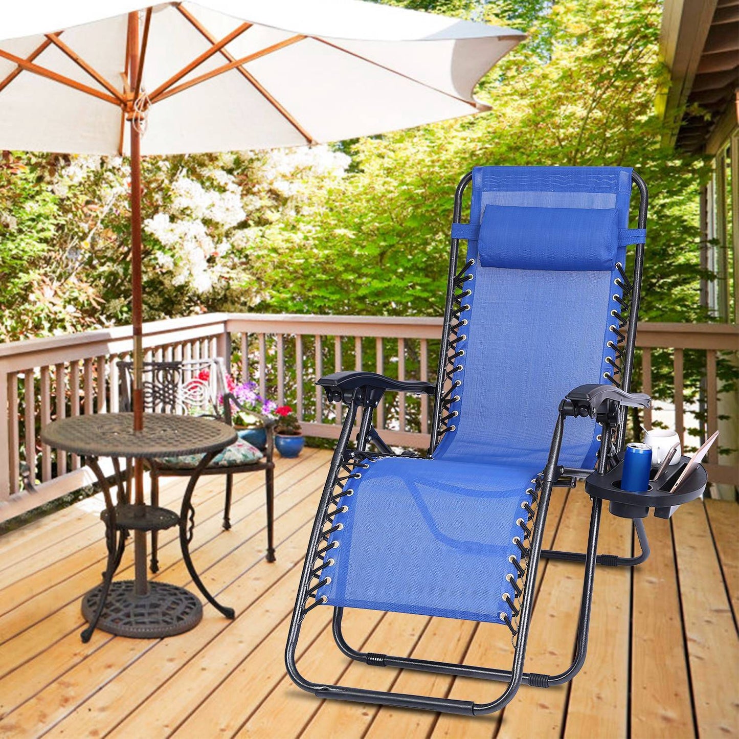 Blue reclining lawn chair with a headrest and cup holder, set on a wooden deck with a patio umbrella and a small table, surrounded by lush greenery.