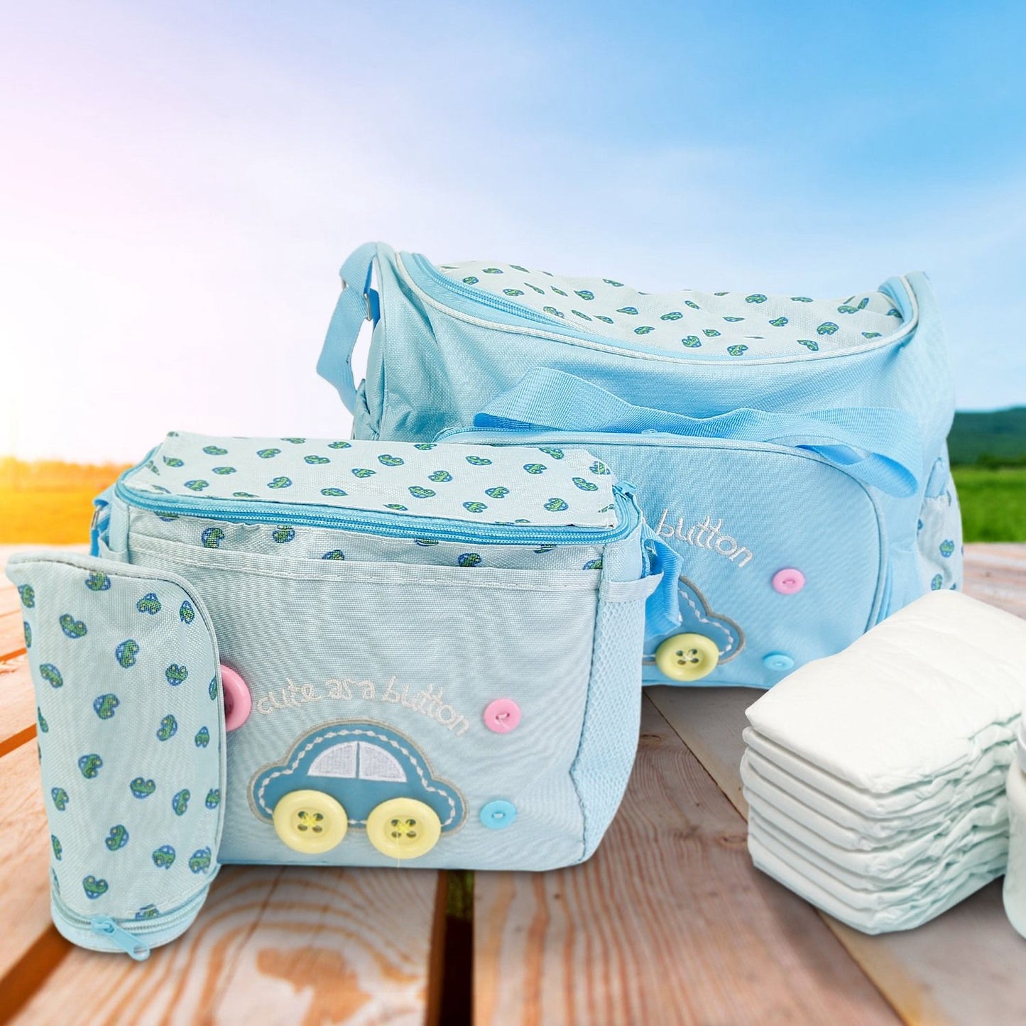 Light blue baby diaper bag set featuring a whimsical car design, polka dot patterns, and buttons, placed on a wooden surface with diapers beside it, against a bright outdoor background.