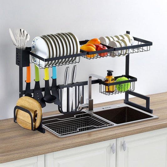 Multi-tier kitchen sink organizer with drying rack, plates, fruits, utensils, and dishware displayed on a wooden countertop.