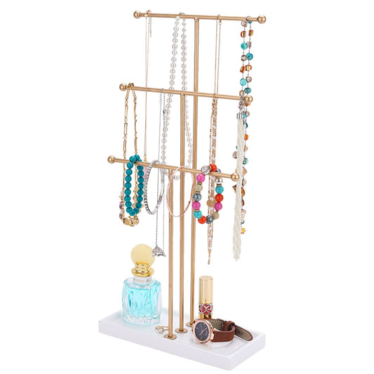 Gold jewelry organizer stand displaying colorful necklaces, bracelets, and a watch, with a decorative perfume bottle and lipstick on a white base.