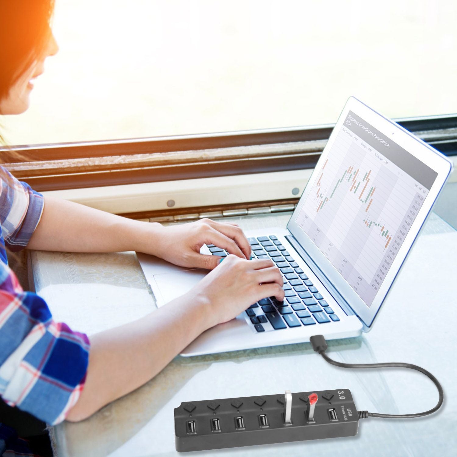 USB power strip with multiple ports, showcased while a person uses a laptop at a table with a financial chart on the screen.