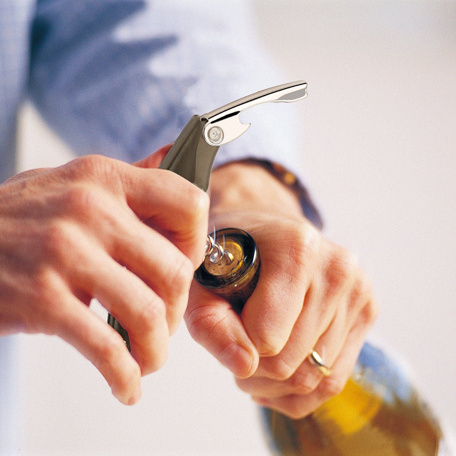 Close-up of a person using a corkscrew wine opener to uncork a bottle, showcasing the tool's sleek design and ease of use.