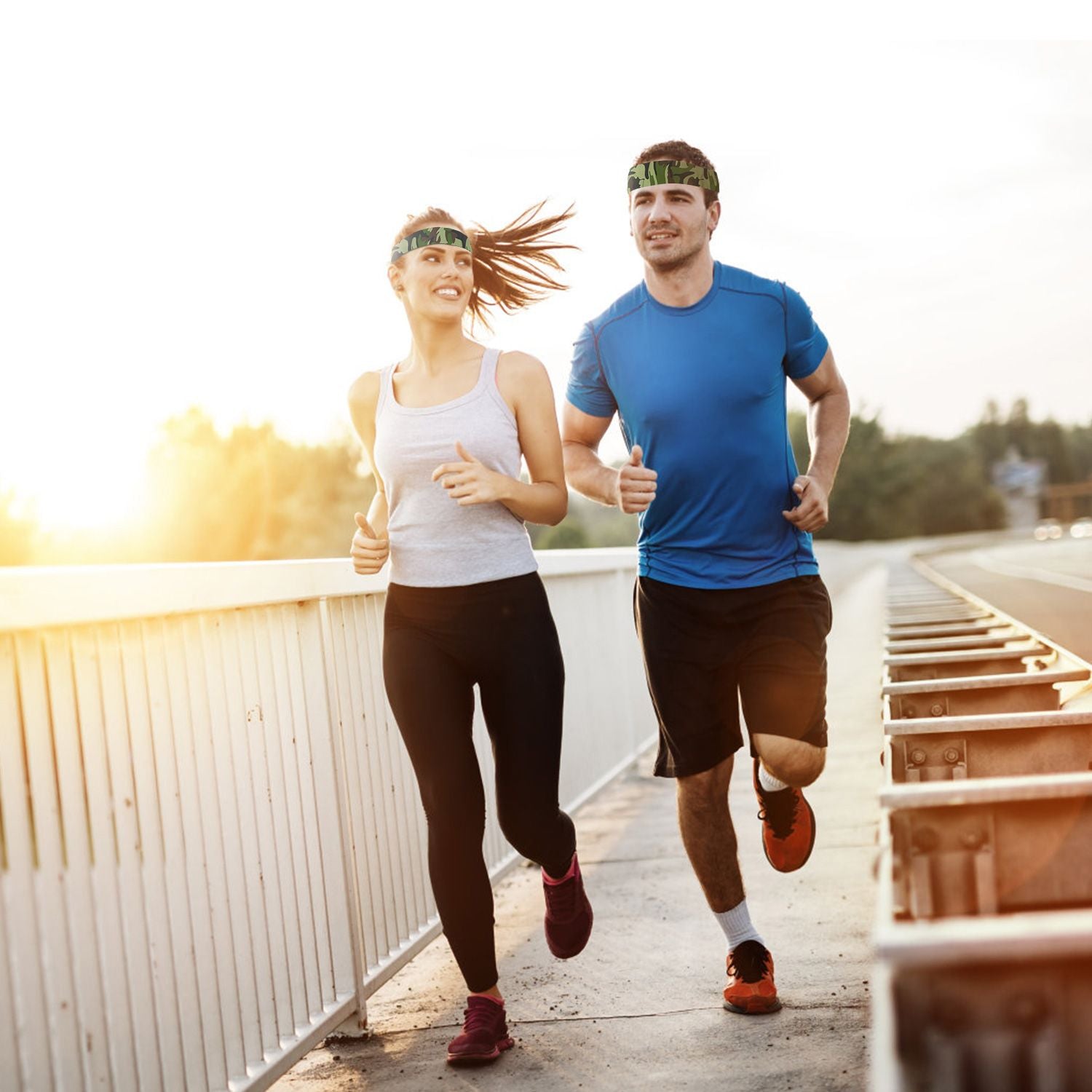 Two runners, a woman in a grey tank top and black leggings, and a man in a blue shirt and black shorts, jogging on a sunny day along a bridge with a scenic backdrop.