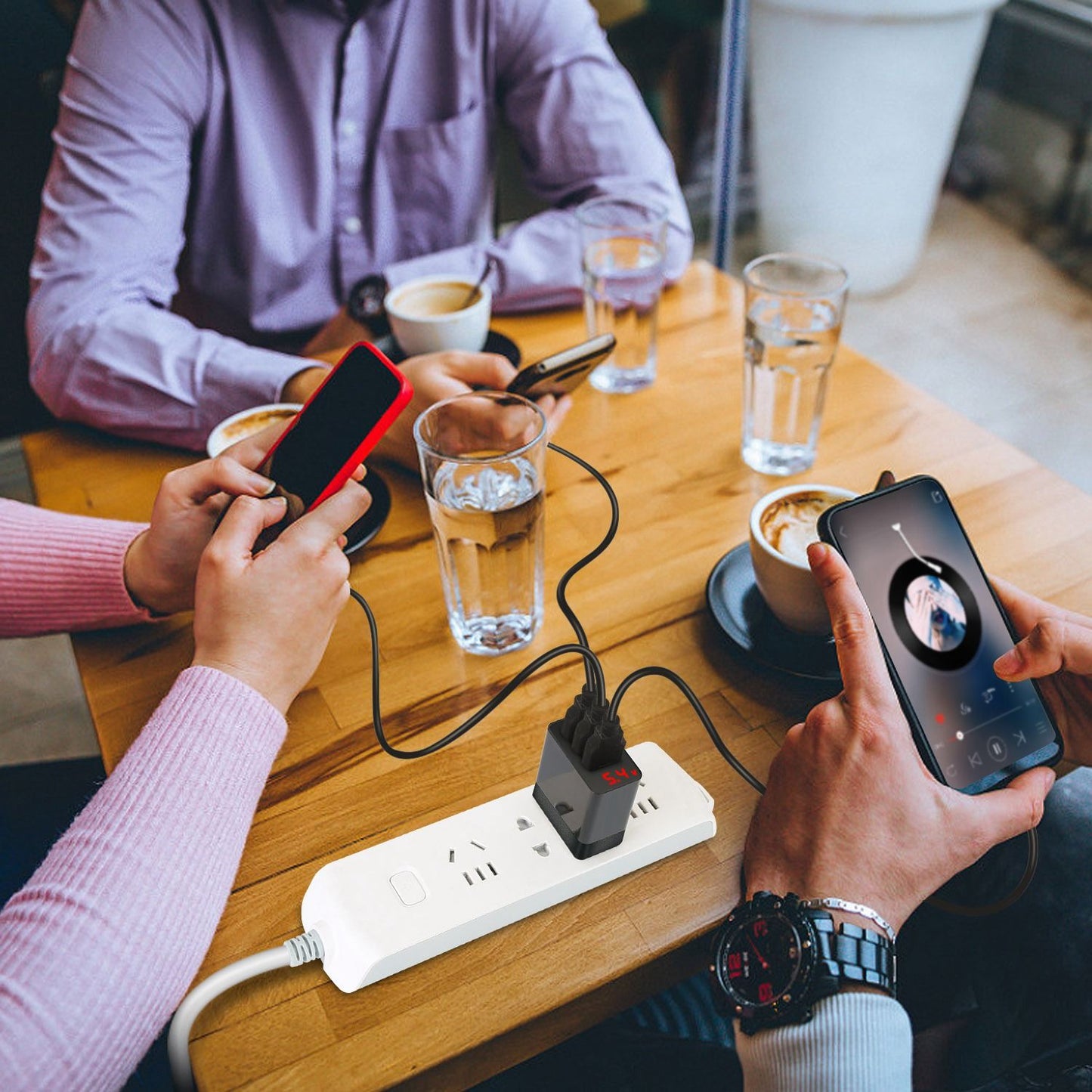 Group of people using smartphones at a café table with a power strip charging devices while enjoying coffee and water.