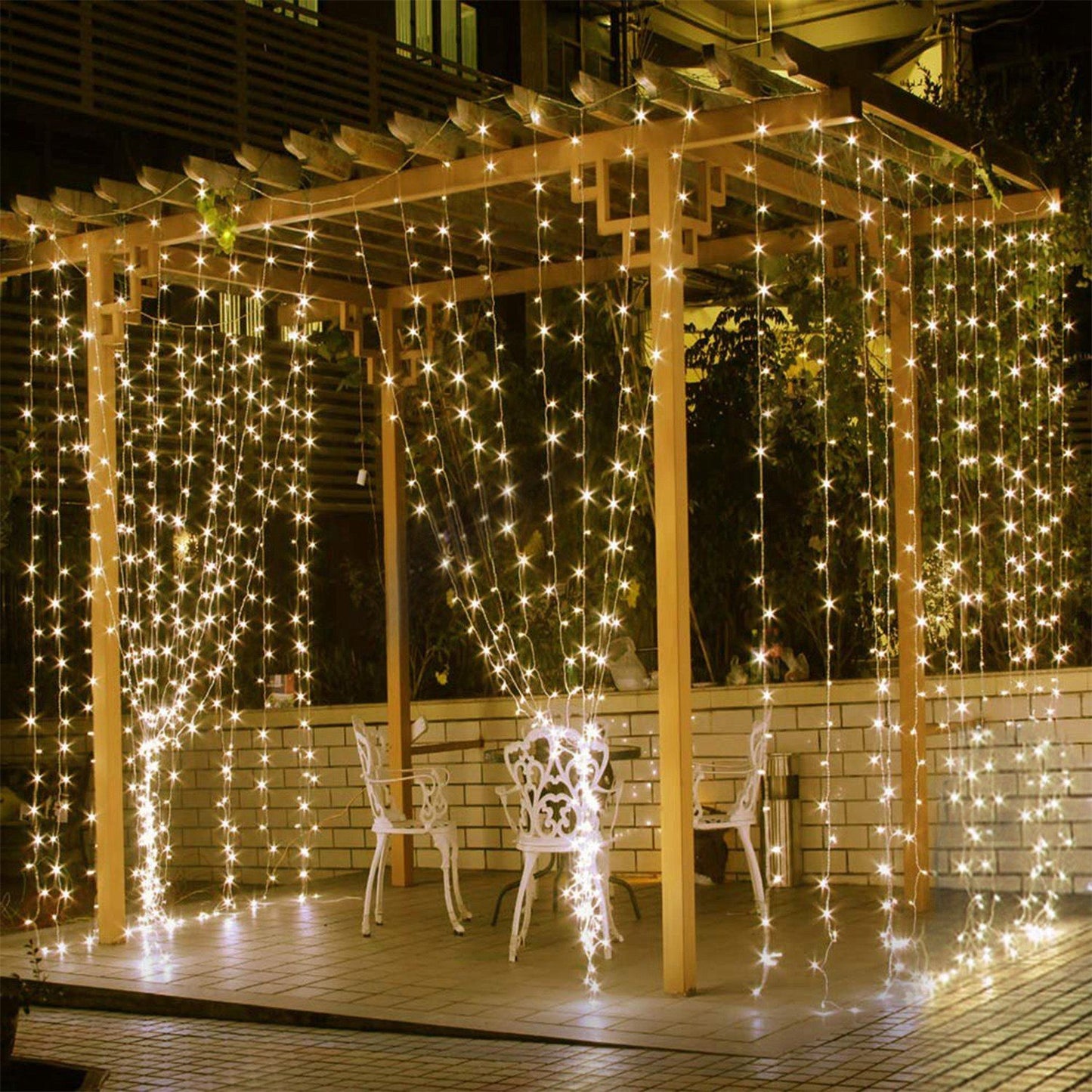 Twinkling LED string lights cascading down a wooden pergola, illuminating a cozy outdoor seating area at night.