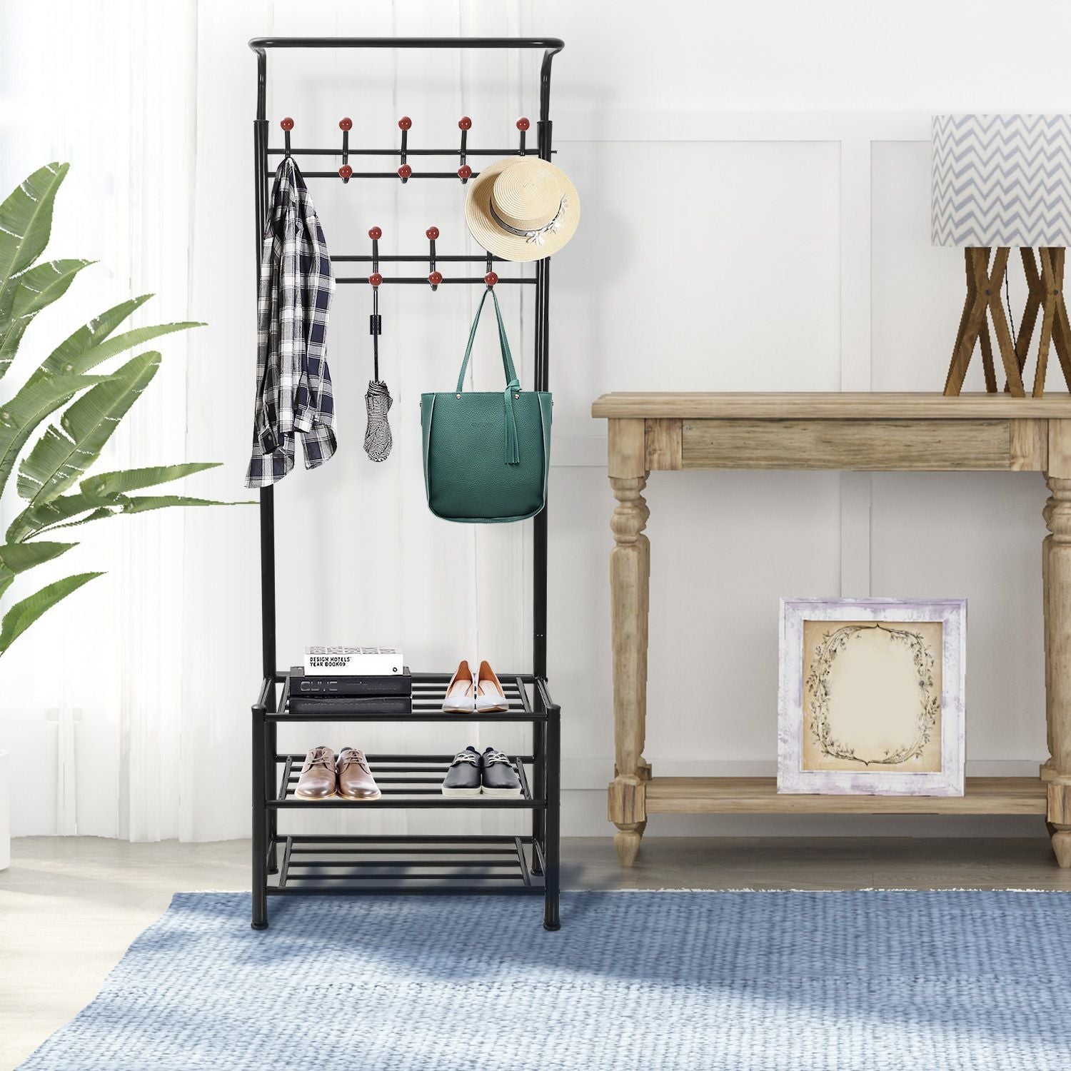 Stylish black entryway coat rack with hooks, hanging accessories, and a shoe storage shelf, complemented by a green bag and a bright indoor setting.