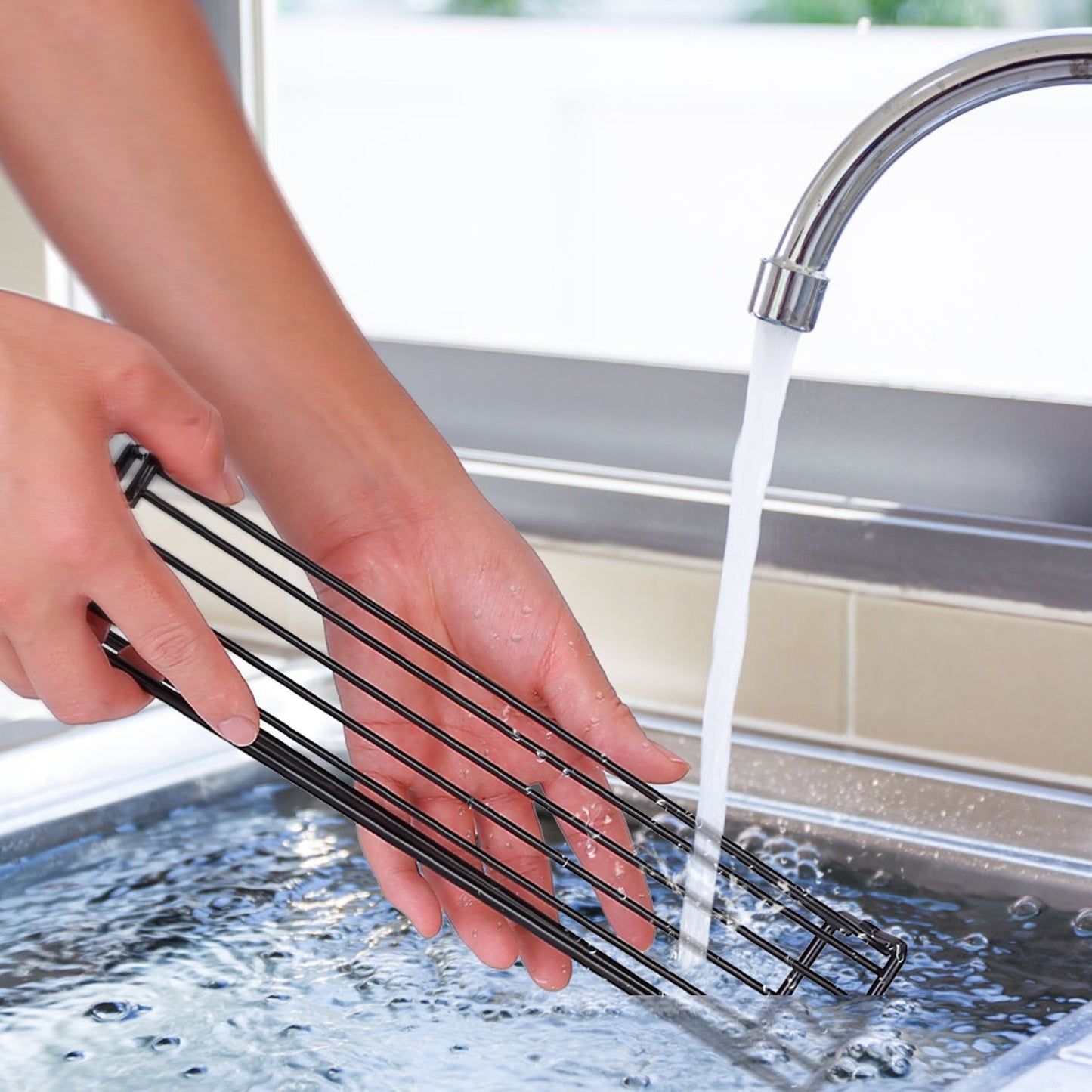 A person rinsing a black grill rack under running water in a kitchen sink, demonstrating easy cleaning of grill accessories.