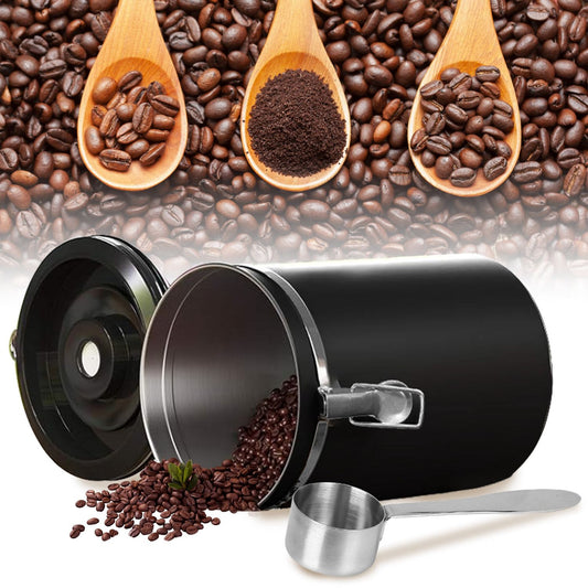 Black coffee storage canister with coffee beans spilling out, alongside wooden spoons filled with whole beans and ground coffee, and a metallic measuring scoop.