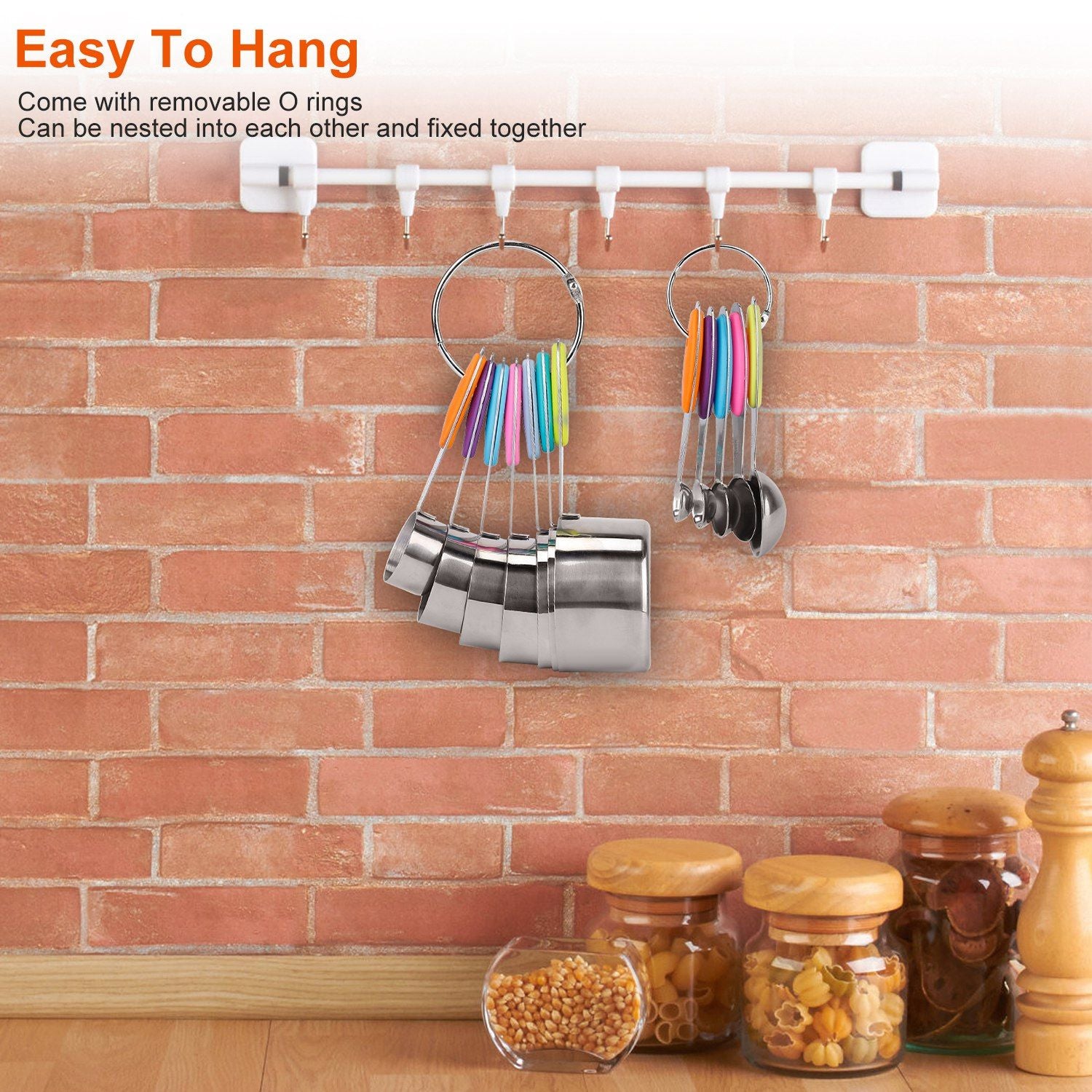 Stainless steel measuring cups and colorful measuring spoons displayed on a wall-mounted rack in a kitchen setting with a brick background, showcasing easy organization and accessibility.
