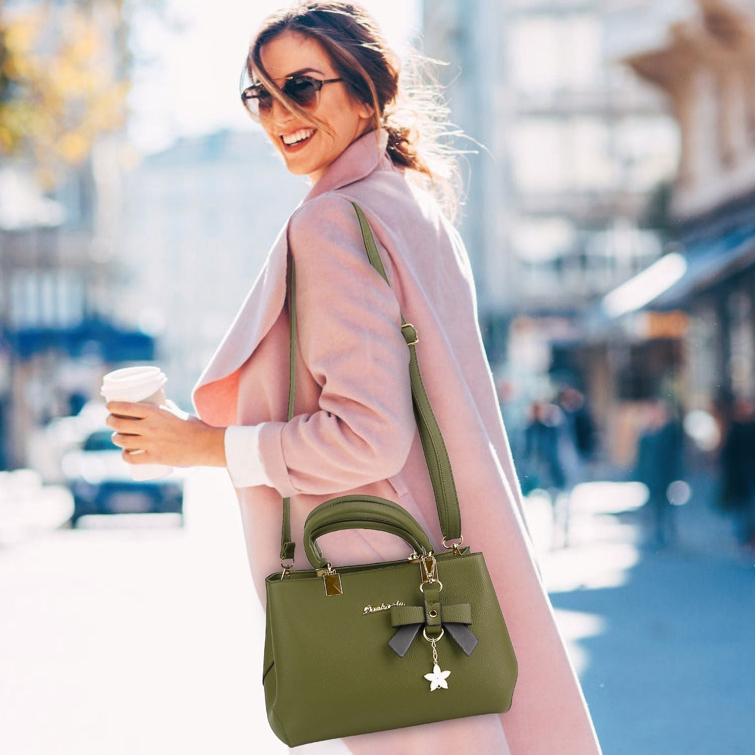 Stylish green handbag with bow and star charm, carried by a woman in a pink coat while holding a coffee cup in an outdoor urban setting.