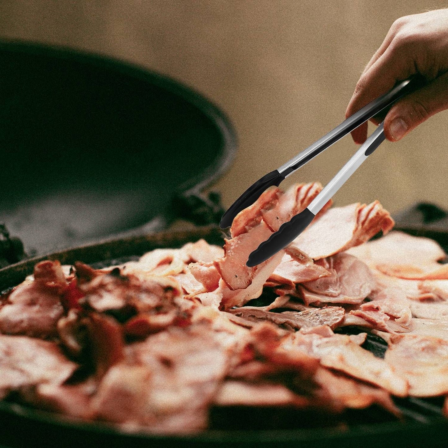 A hand using stainless steel tongs to lift slices of cooked bacon from a pan filled with crispy bacon strips.